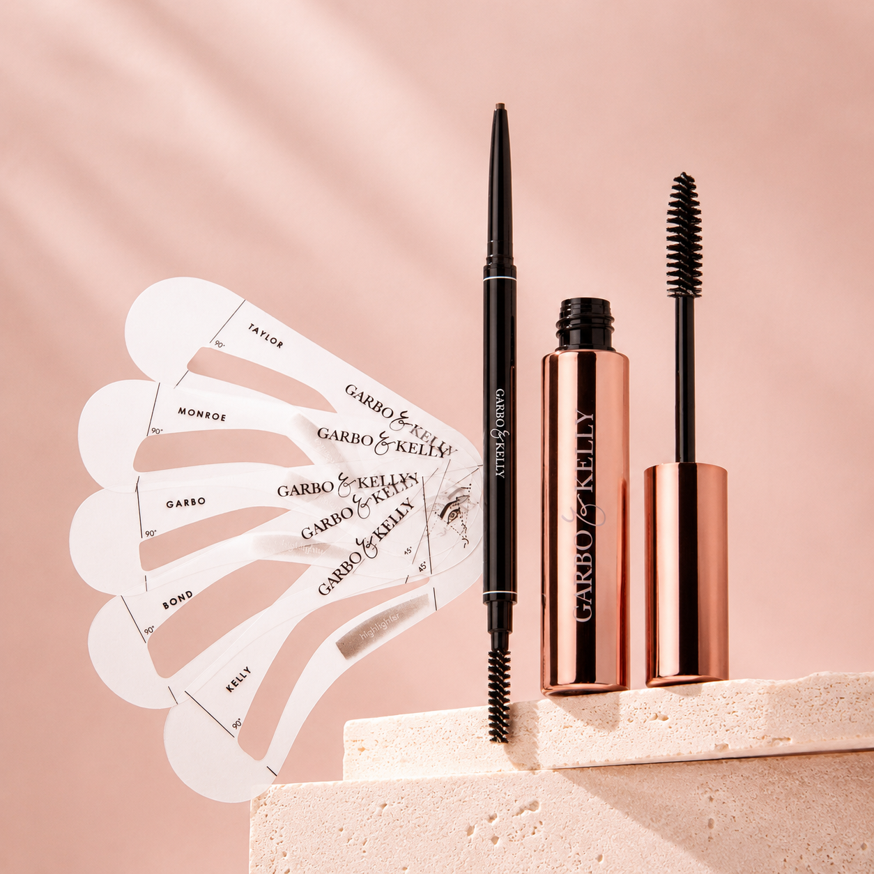 GABRO & KELLY brow set with a black dual-ended pen-style applicator, a rose gold tube, a wand, and white fan-shaped swatch cards on a soft blush background.